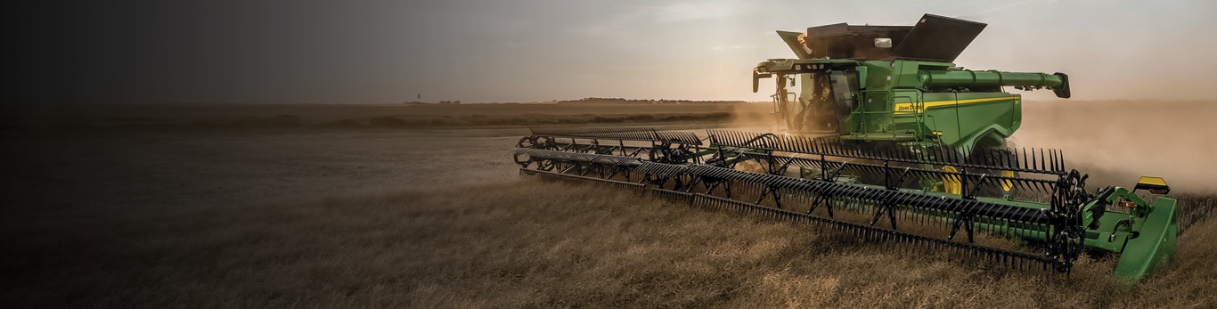 John Deere Harvester harvesting wheat during sunset