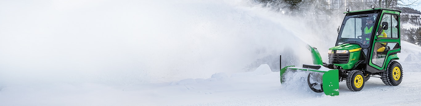 A landscaping operator blowing snow on a John Deere X700 Signature Series lawn tractor.