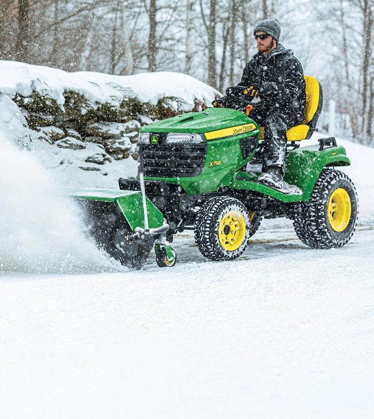A landscaping operator blowing snow on a John Deere X700 Signature Series lawn tractor.