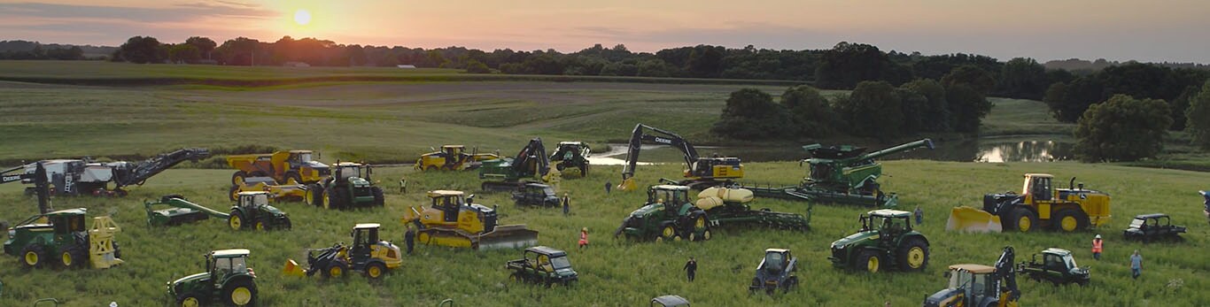 Des gens se promenant parmi plusieurs types d’équipement John Deere dans un grand champ.