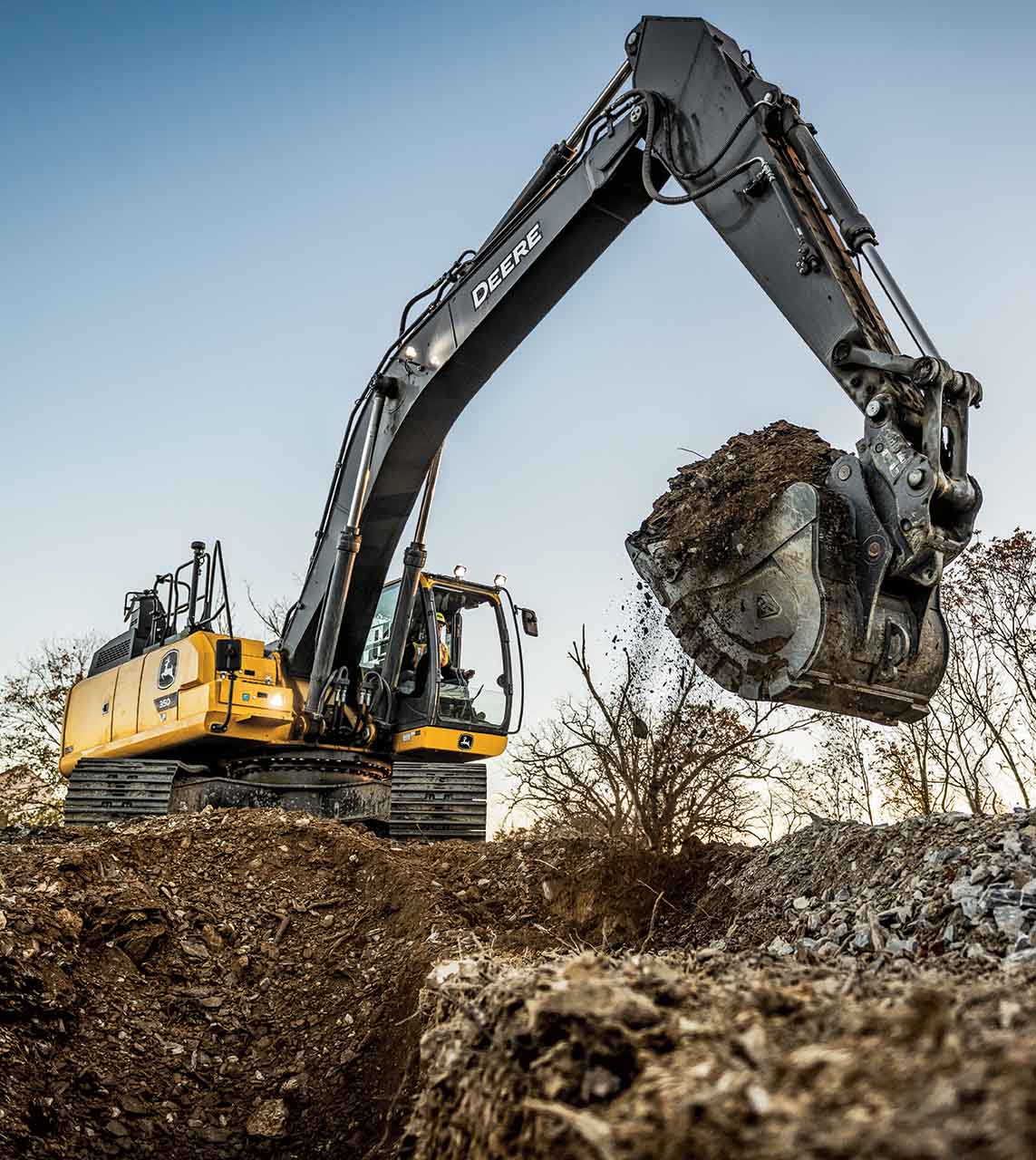John Deere excavator powerfully lifts a bucket overflowing with dirt