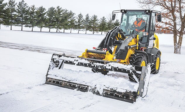 Compact wheel loader with snow removal blade attachment clearing pavement