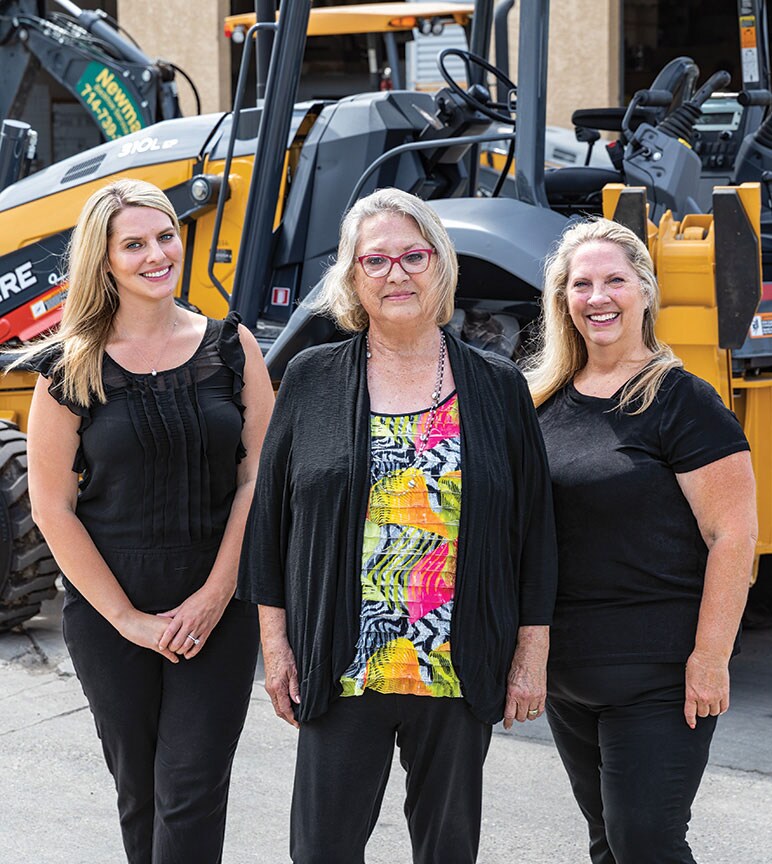 Amanda Matson, Janet Ferguson et Nikki Worden de Newman Backhoe Service se tiennent devant une rétrocaveuse 310L de John Deere.