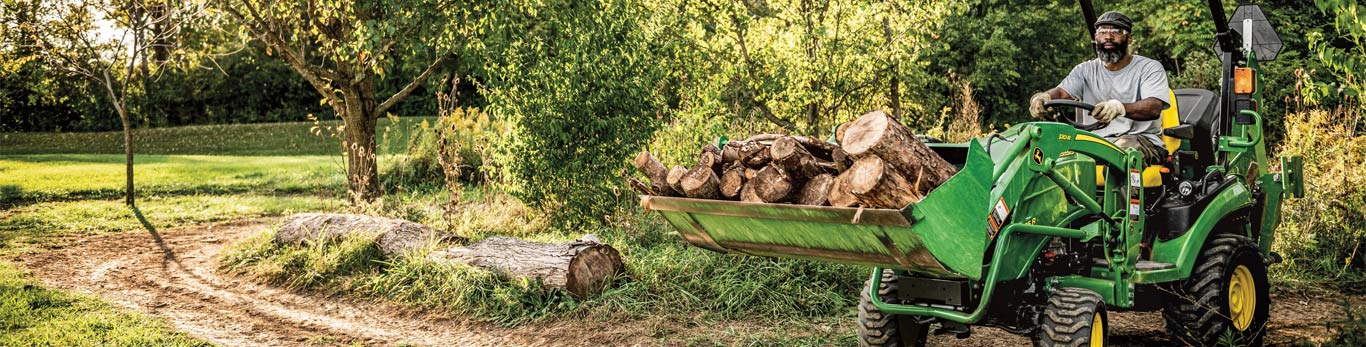 Man driving a Compact Tractor with a loader full of logs
