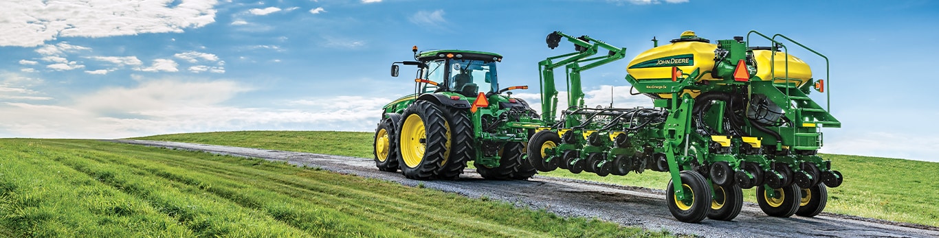 a deere tractor and sprayer system driving down a gravel path in a grass field