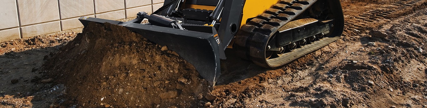 329D Compact Track Loader with Dozer Blade attachment pushing dirt next to a building.