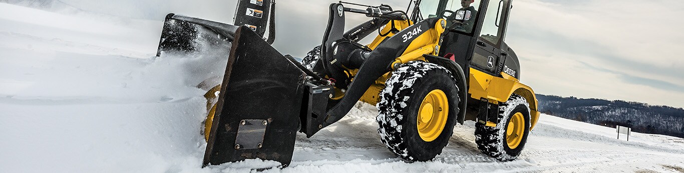 Chargeuse compacte&nbsp;324K &eacute;quip&eacute;e d&rsquo;une souffleuse &agrave; neige chassant la neige d&rsquo;une route