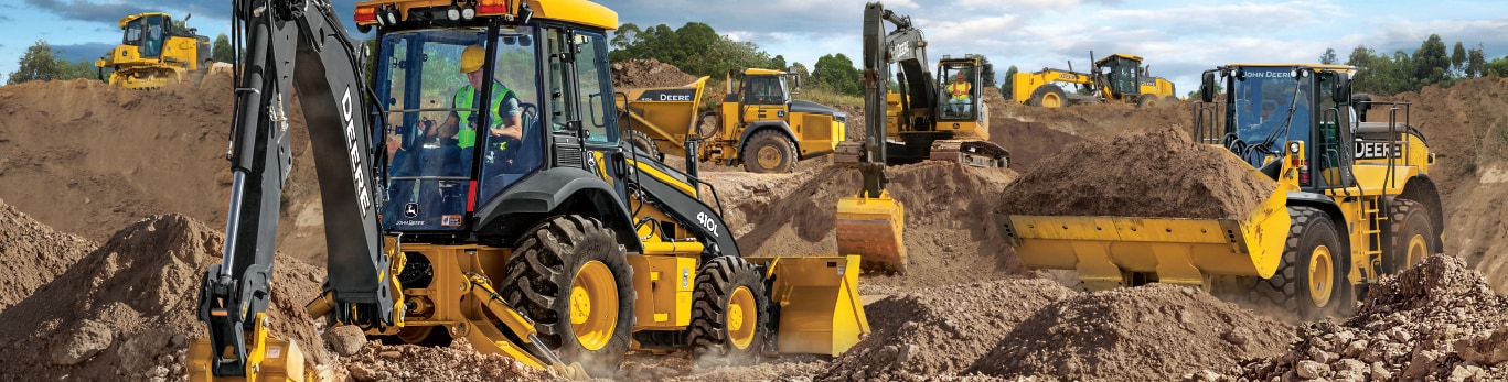 Multiple types of John Deere heavy and compact construction equipment working in dirt.