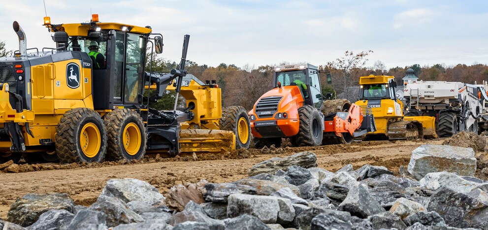 Une niveleuse automotrice John Deere, un rouleau Hamm, un bouteur John Deere et une machine de voirie Wirtgen construisant une nouvelle route