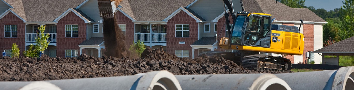 Grande rétrocaveuse chenillée creusant une tranchée pour des tuyaux en béton dans une zone résidentielle