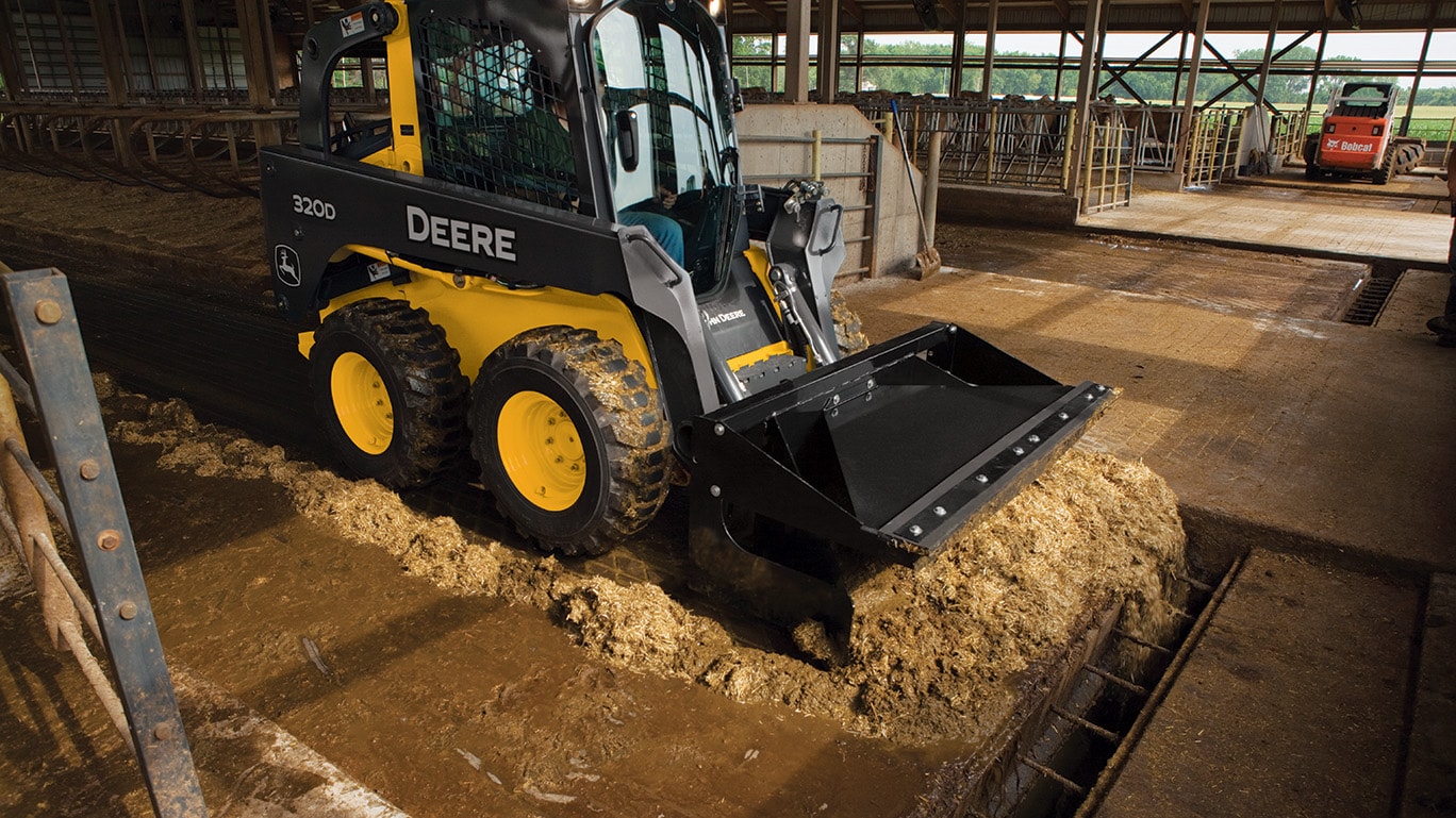 320D Skid Steer with material scraper working in a livestock confinement