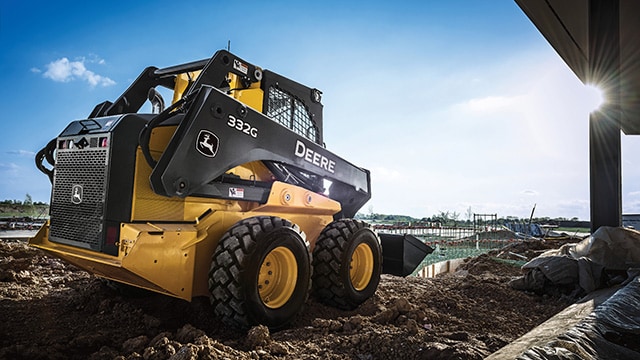 Chargeur compact John Deere 332G travaillant sur un chantier de construction commercial.