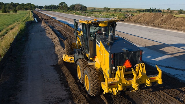 John Deere motor grader is leveling dirt at a roadbuilding site.