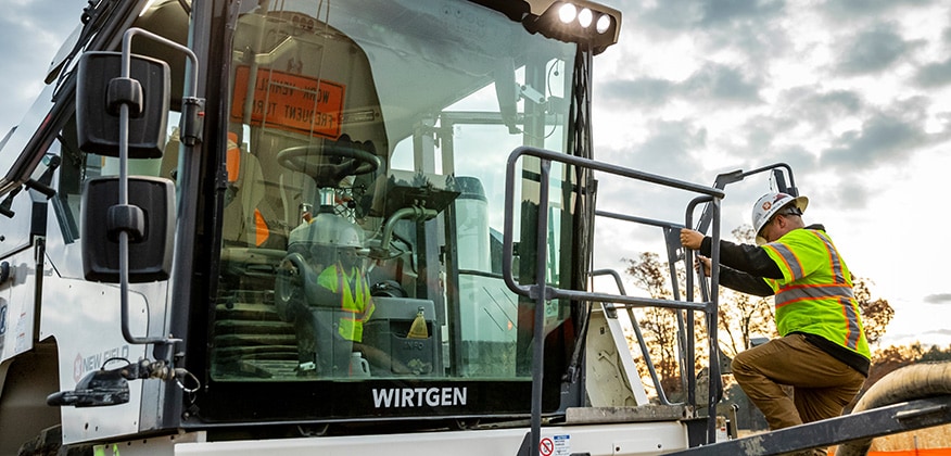 Un opérateur de machinerie qui monte dans la cabine du broyeur mobile à mâchoires Wirtgen KLEEMANN.