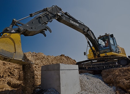 The word “underground” is on top of a John Deere 245 P-Tier Excavator and 524 P-Tier Wheel Loader working behind a stack of blue water pipes at a new development site.