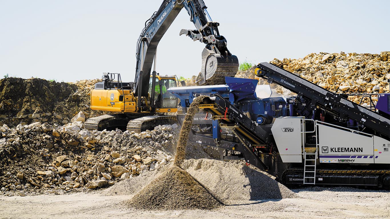 Excavatrice déversant de l’asphalte concassé dans un concasseur mobile Kleemann