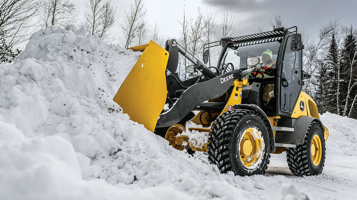 John Deere compact wheel loader using bucket attachment to move snow.