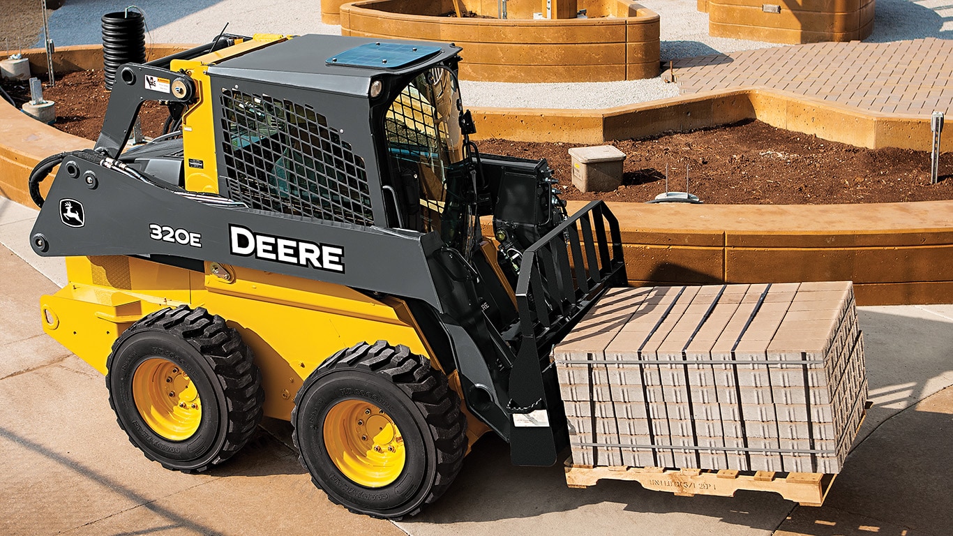 320E Skid Steer with pallet forks attachment, hauling a pallet of blocks.