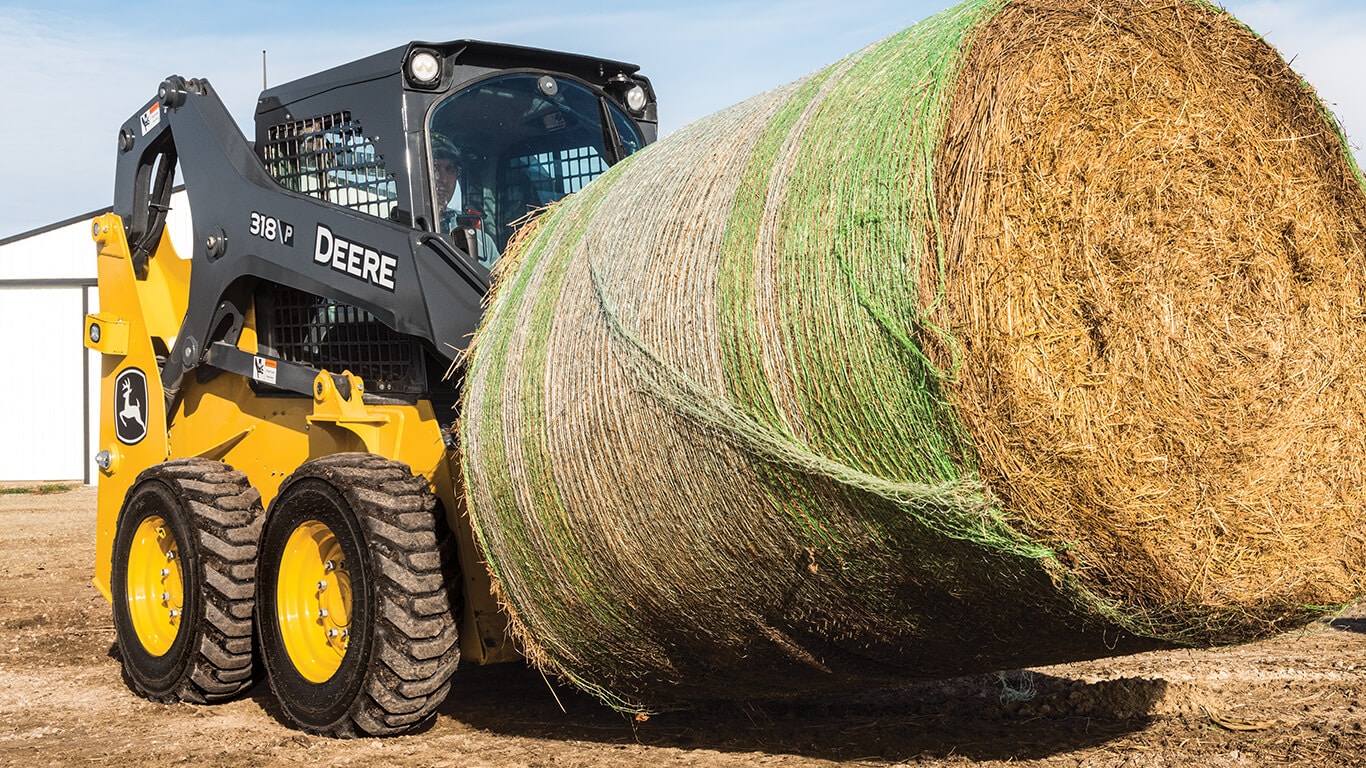 318 P-Tier skid steer lifting and moving hay bale with Deere fork attachment.