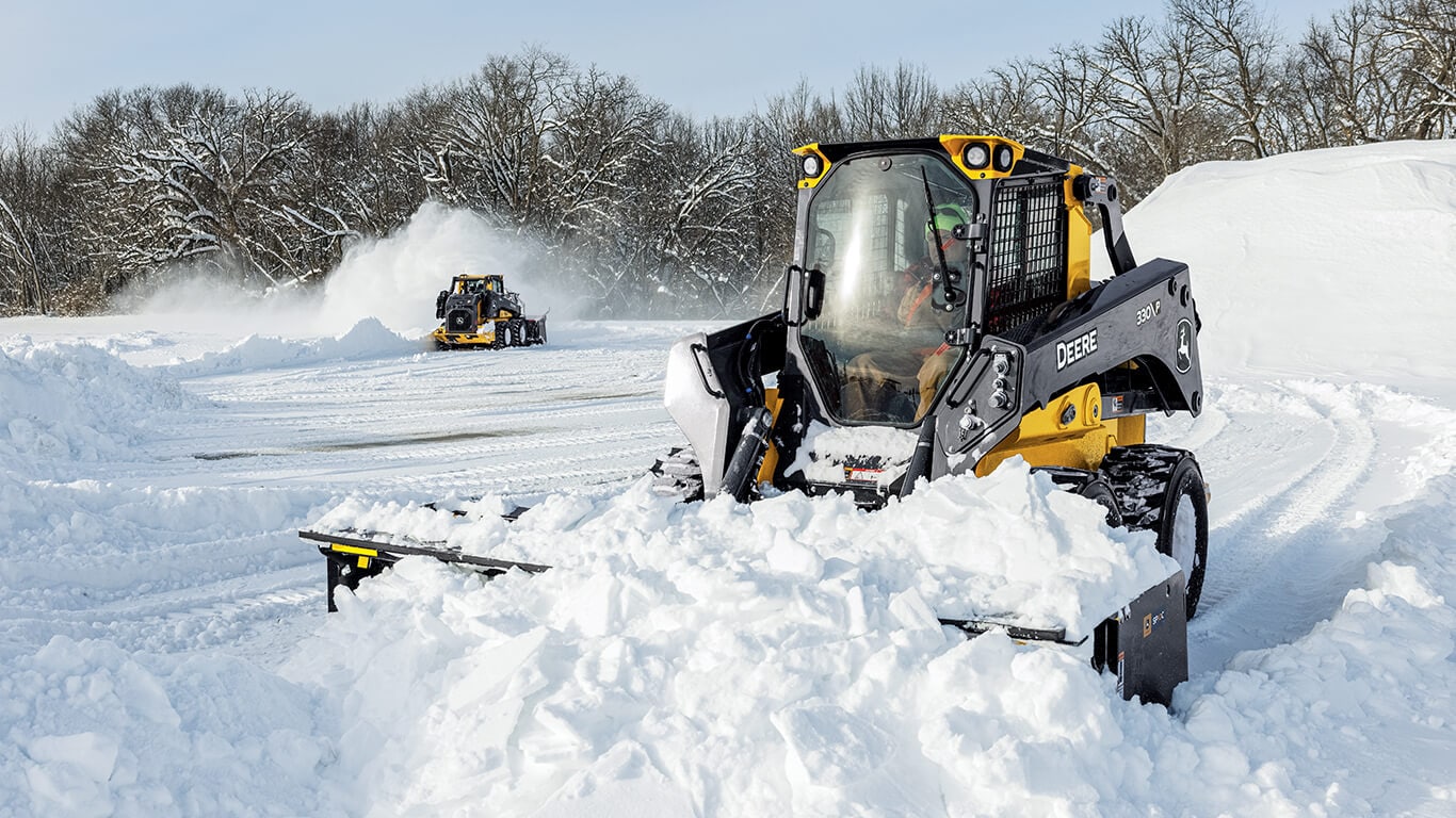 330 P-Tier skid steer moving snow with Deere snow pusher attachment.