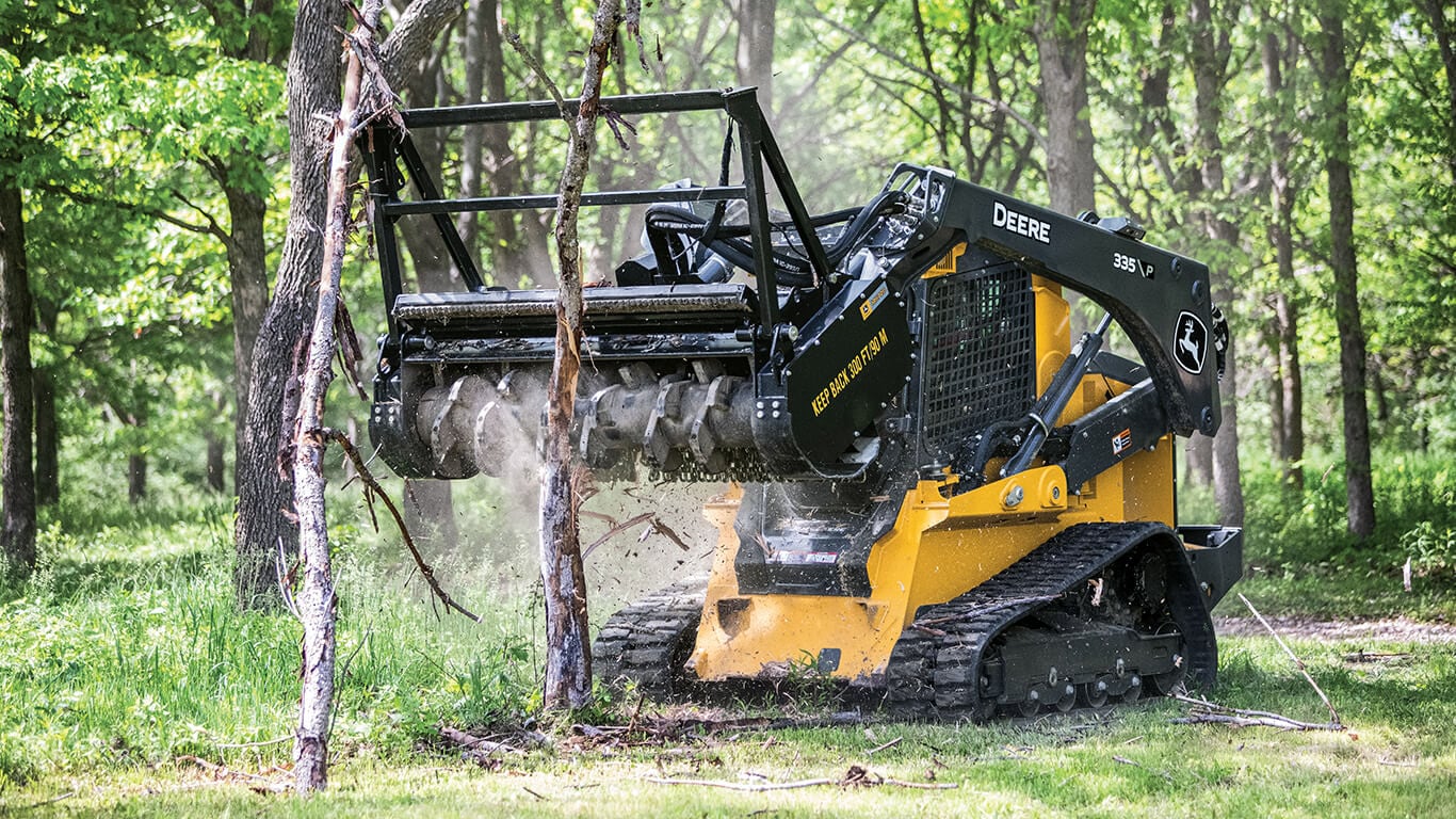 John Deere 333G compact track loader clearing branches using a John Deere grapple attachment.