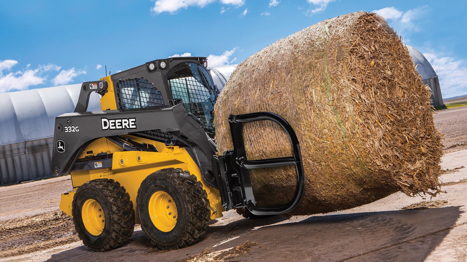 332G Skid Steer with bale hugger attachment driving through a concrete lot on a farm