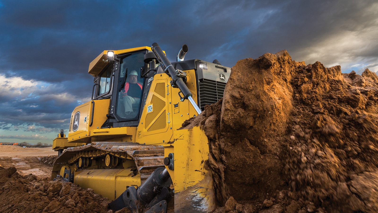 850L Dozer pushes a pile of dirt in front of a dramatic clouded sky
