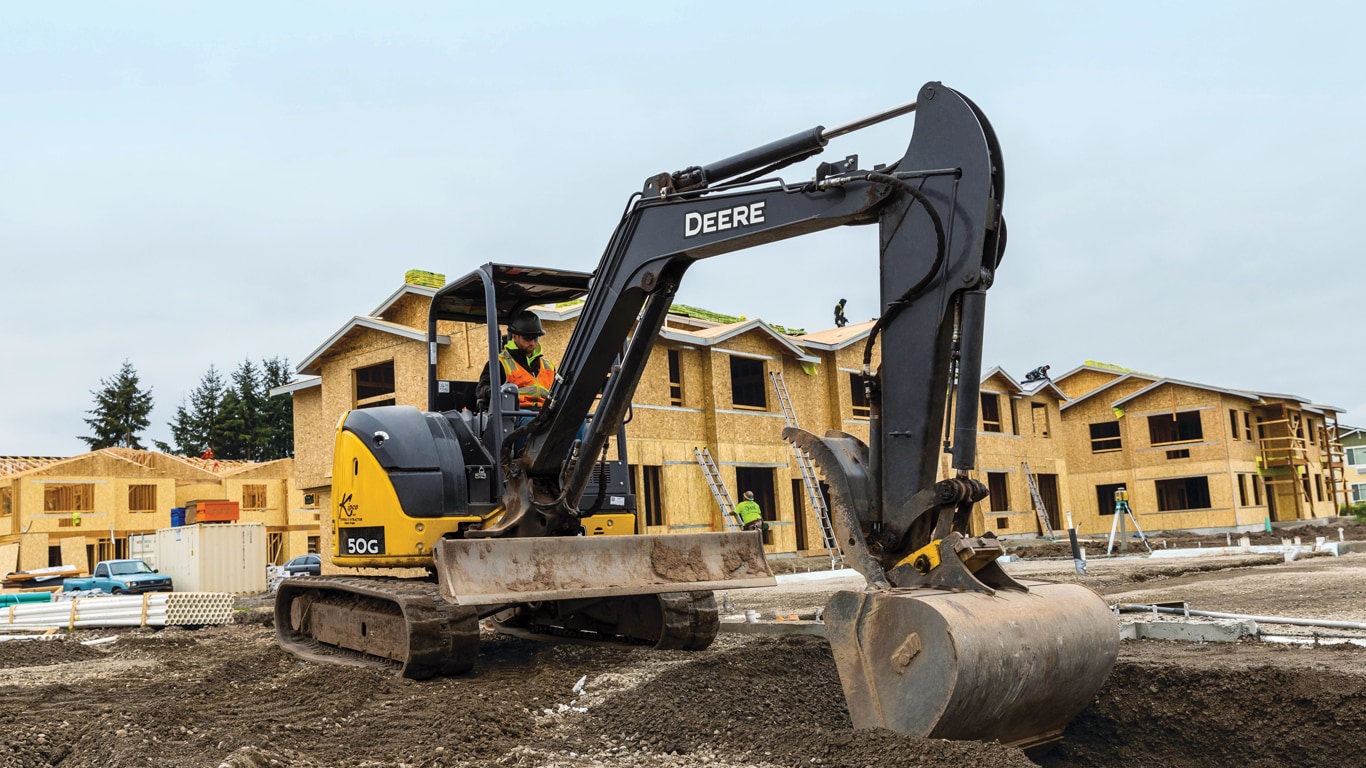 Excavatrice compacte 50G creusant sur un chantier avec des appartements inachevés à l’arrière