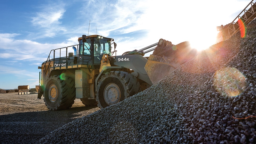 John Deere 944k hybrid loader dumping a load of rocks into a dump truck at a quarry
