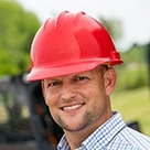 Construction worker in a red hardhat with work site in the background