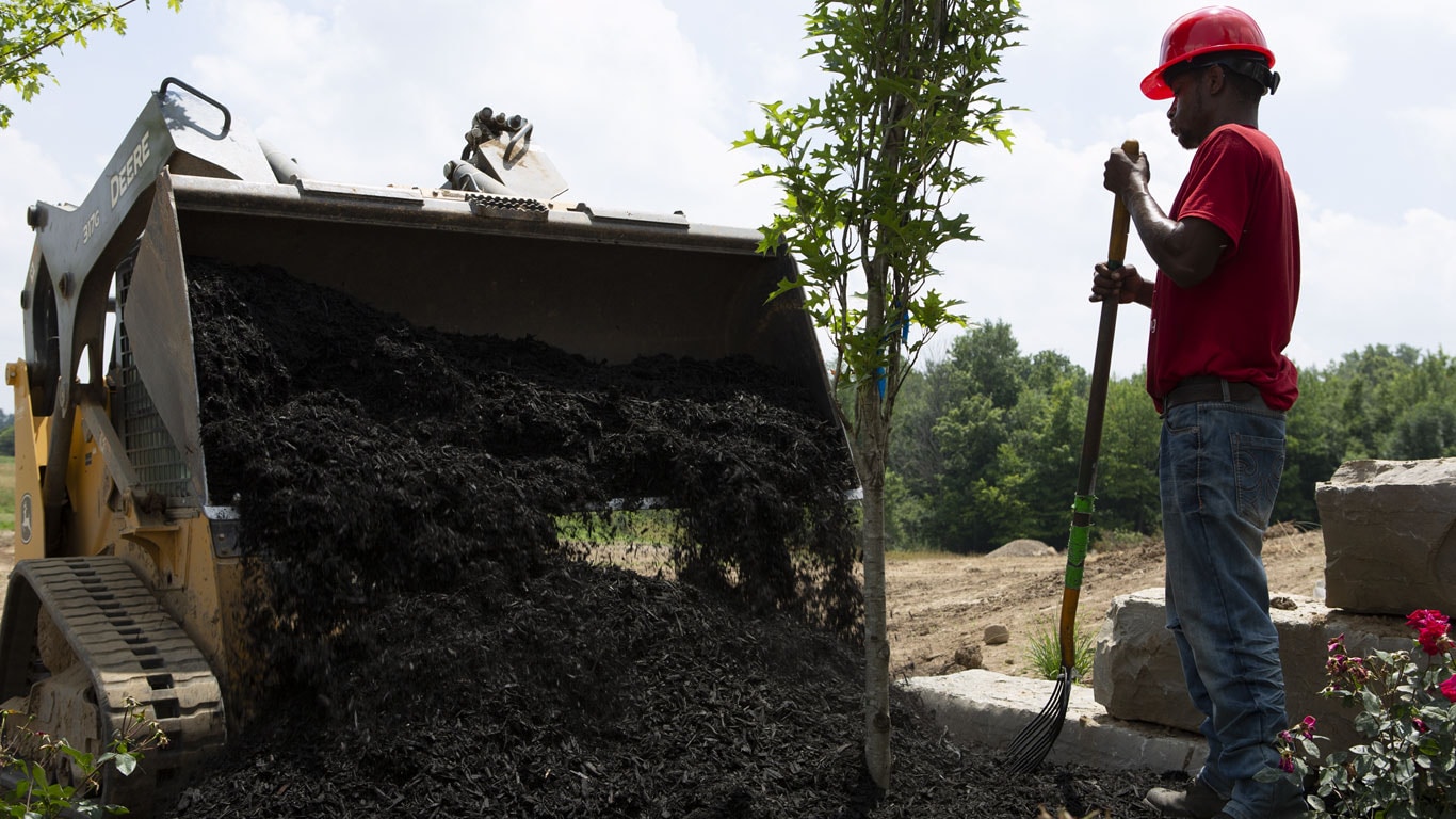 The 317G with a load of soil and a worker on a landscaping site.