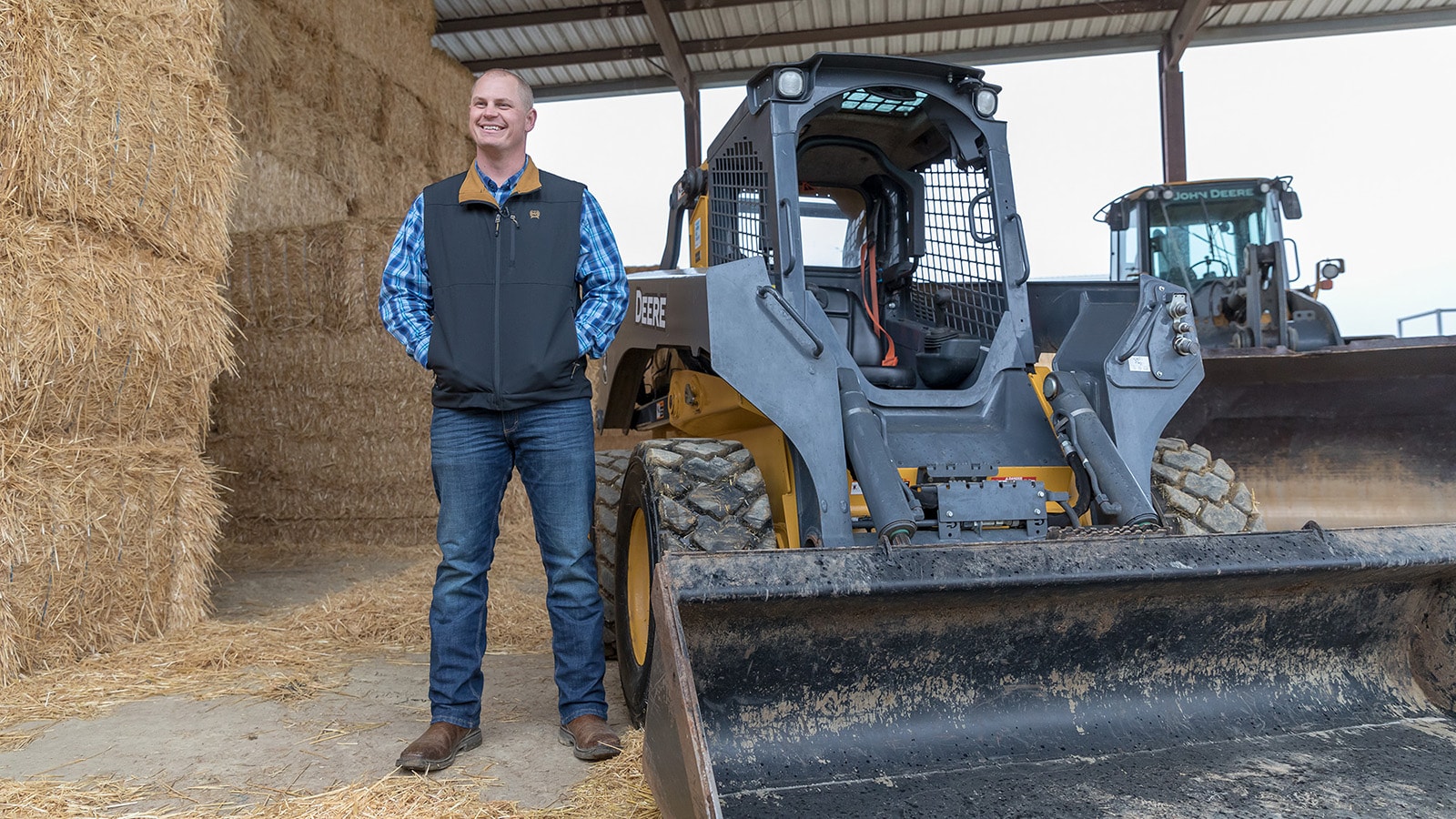 John Verwey stands next to his 332G Skid Steer with bales of hay in the background