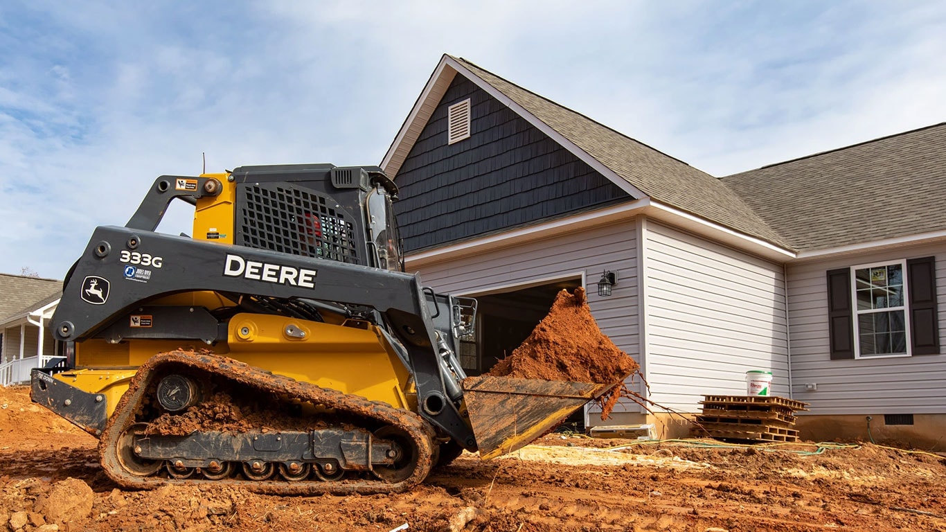 A 333G hauls a load of dirt in from of a house under construction