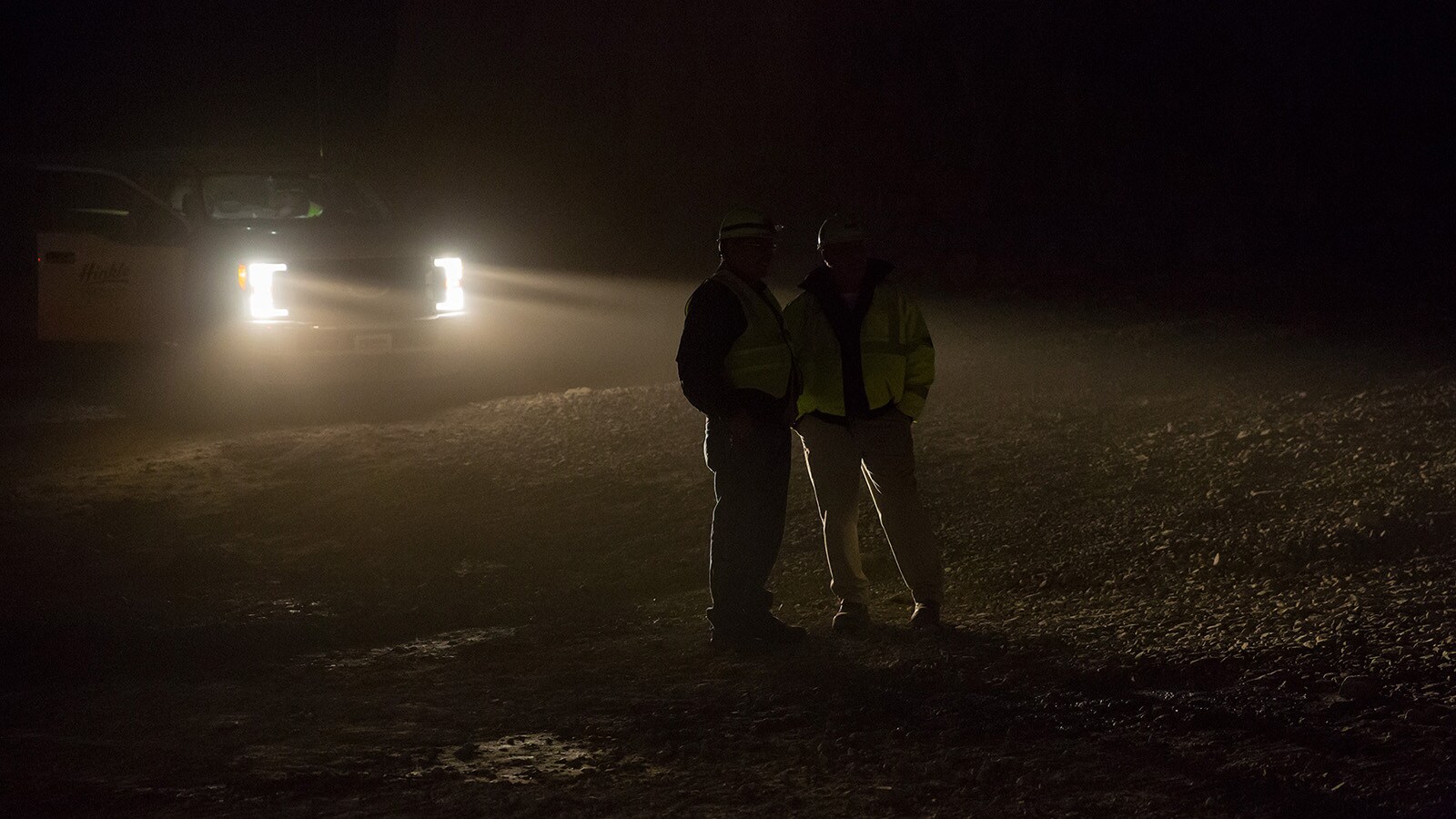 Two workers talk in the headlights of a pickup truck in the mine