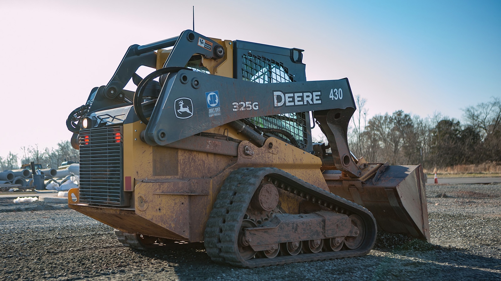 325G Compact Track Loader, covered in dirt and mud, drives across a gravel lot