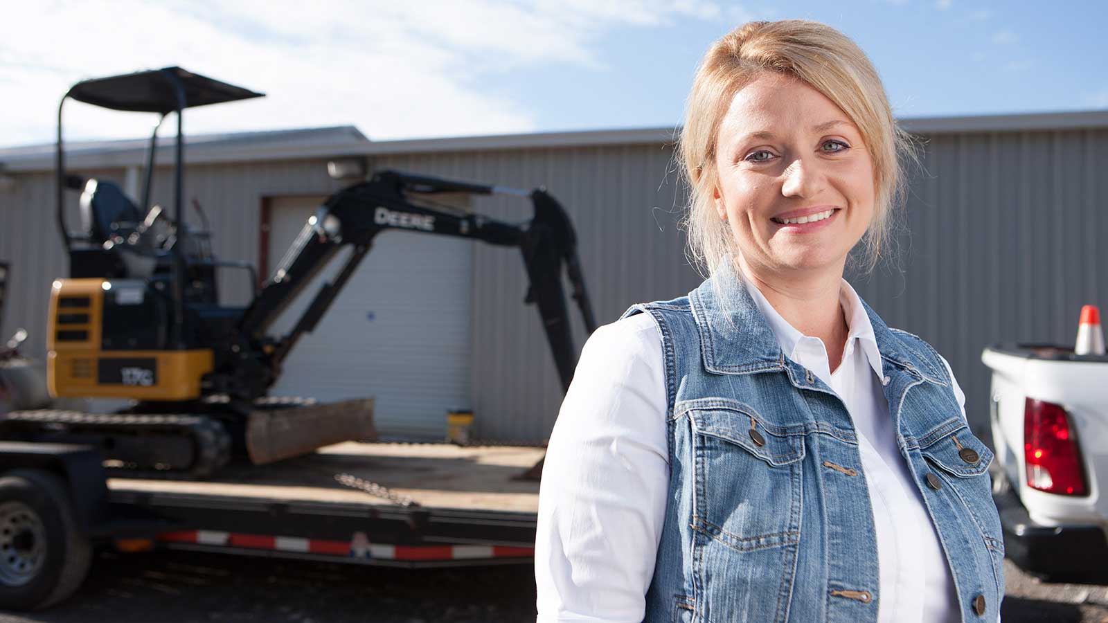 Chasity Crowe-Moore stands in front of a 17G mini excavator on a trailer.