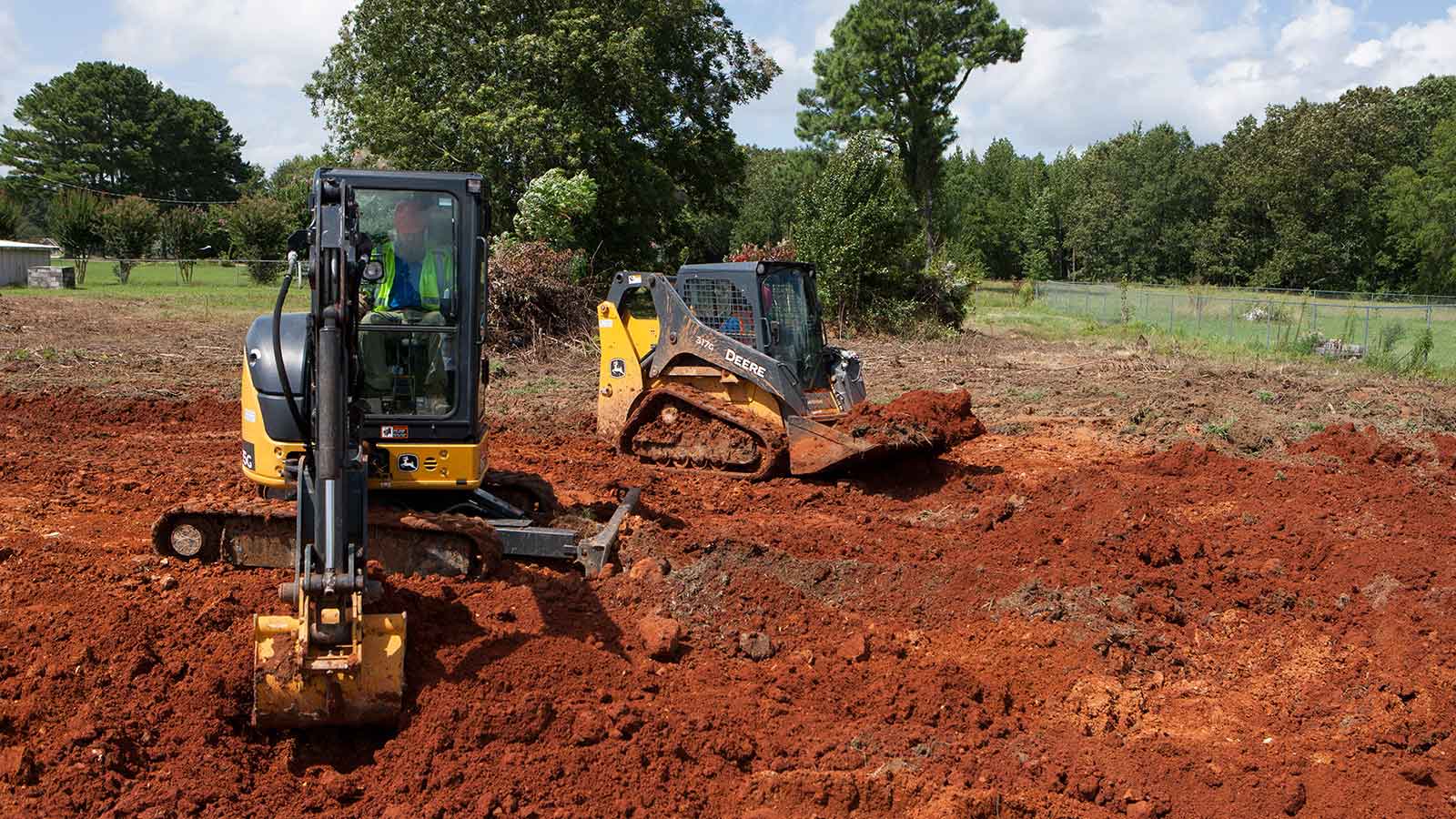 A John Deere compact track loader and mini excavator on a jobsite.