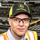 Josh Kempel, Global Sales and Marketing Manager for John Deere Reman, wearing a John Deere hat and safety glasses.