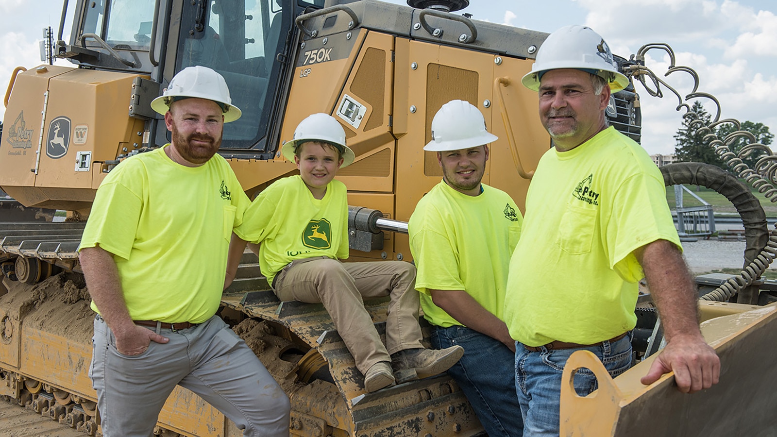 4 people pose for a photo in front of a 750K dozer