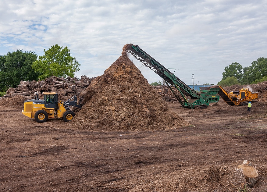 a conveyor drops mulch into a pile, while a wheel loader scoops loads off of the pile