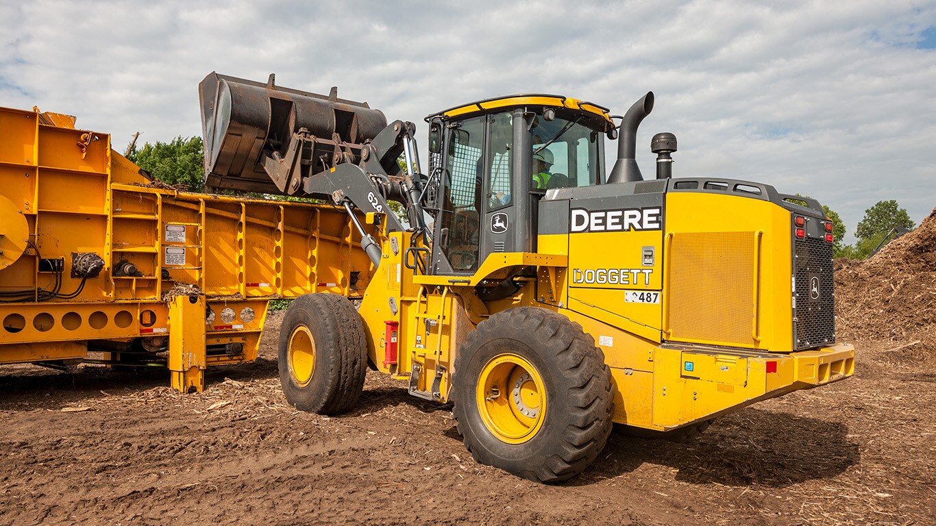 A 624K wheel loader dumps wood scraps into a grinder machine