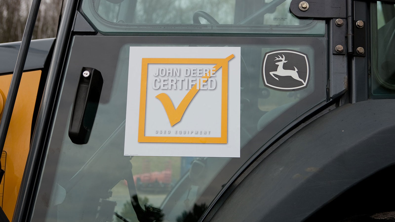 The John Deere Certified Used check mark logo on the window of a loader.