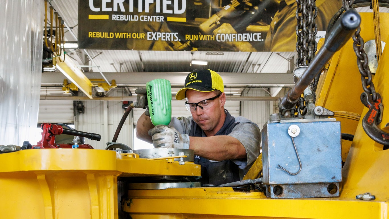 mechanic using a power tool and working on rebuilding a John Deere machine