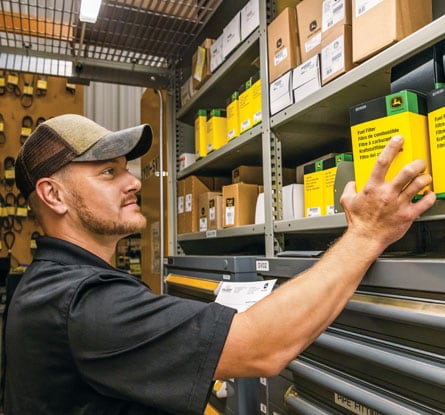 A man reaching for a fuel filter on the shelf of a stock room.