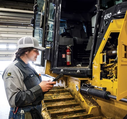 A female mechanic looking into the engine compartment of a John Deere 650 P-Tier Dozer.