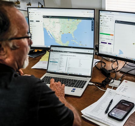 A man sitting at a desk with multiple computers.