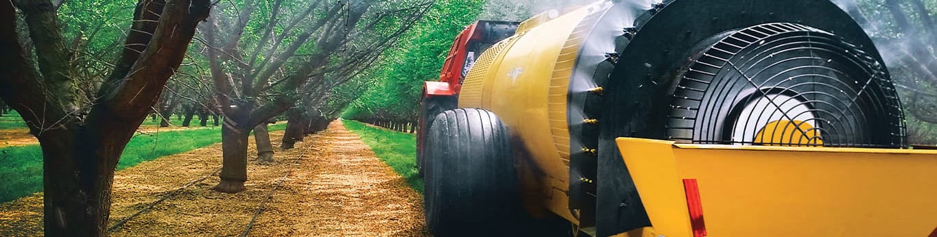 Pulv&eacute;risateur pour verger propuls&eacute; par un moteur John Deere, circulant le long d'une rang&eacute;e d'arbres.