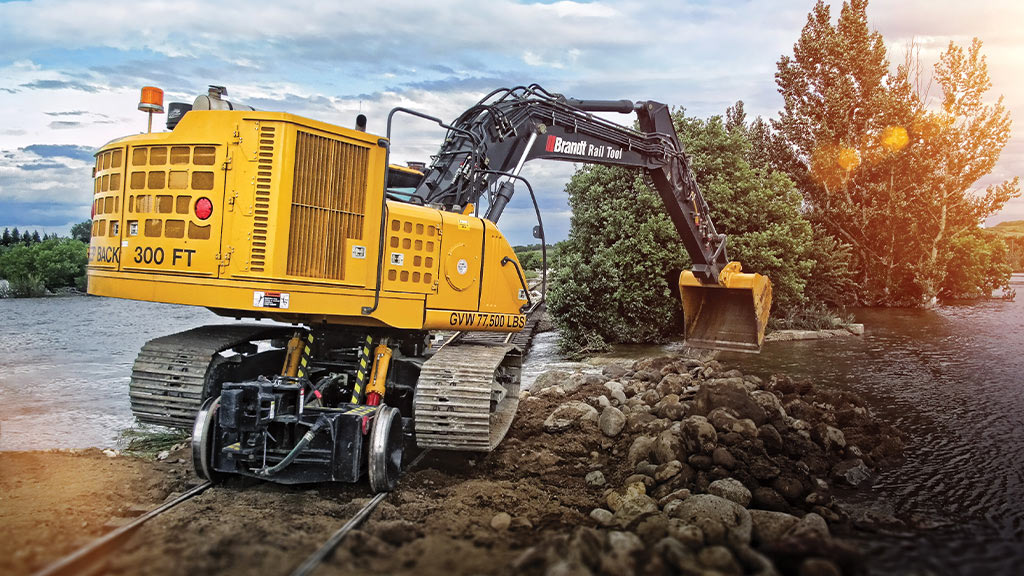 Équipement pour outils sur rail de Brandt alimenté par un moteur industriel John Deere ramassant de la roche dans un cours d’eau.