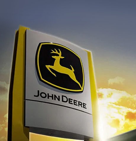 A sign with the John Deere logo sits in front of a building during sunset