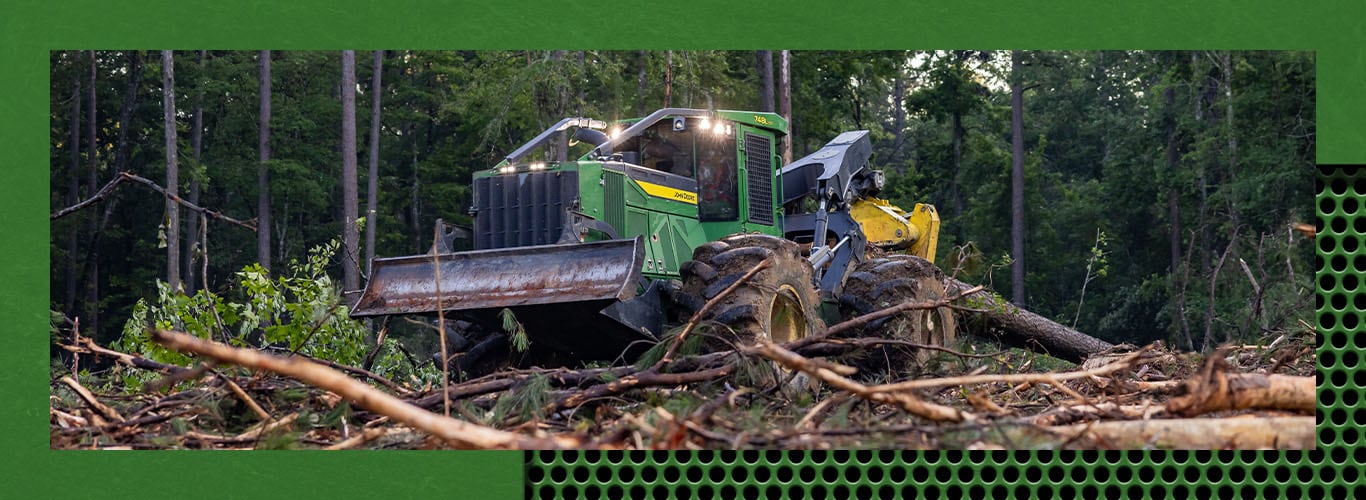 Green forestry skidder moving logs in a forest clearing with trees in the background.